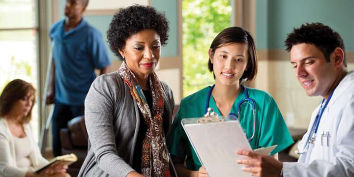 Three doctors and nurses assess a clipboard together